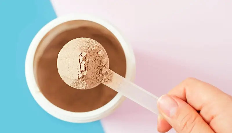 Hand holding a scoop of protein powder over a container with a colorful background