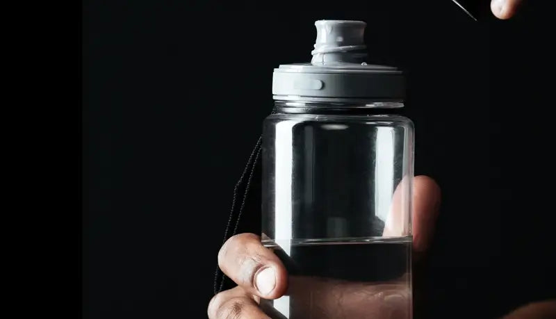 Clear water bottle held by a hand against a black background