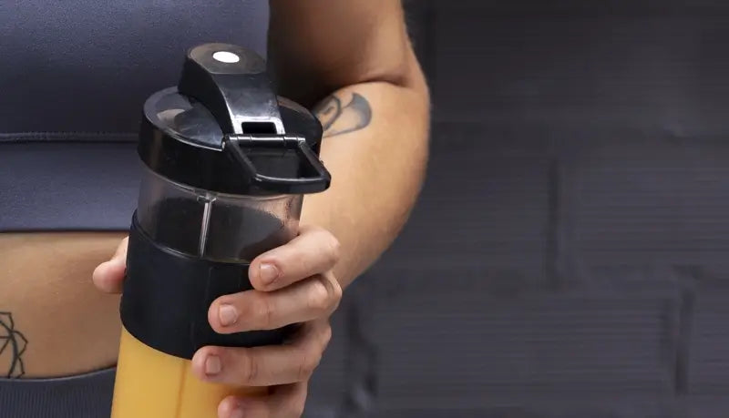 Person holding a black and yellow shaker bottle against a dark background